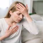 Mulher com a mão na testa e no peito, demonstrando ansiedade.