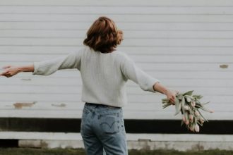 Mulher solteira de costas com flores, em frente a uma parede branca.