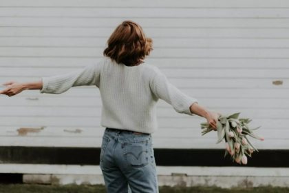 Mulher solteira de costas com flores, em frente a uma parede branca.