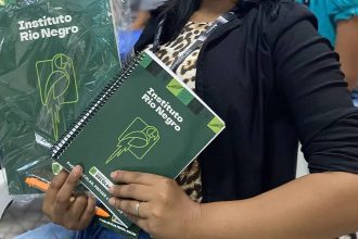 Mulher segura cadernos do Instituto Rio Negro com logotipos, em um evento.
