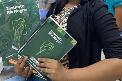 Mulher segura cadernos do Instituto Rio Negro com logotipos, em um evento.