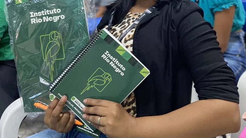 Mulher segura cadernos do Instituto Rio Negro com logotipos, em um evento.