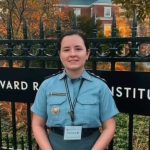 Oficial da Polícia Militar do Amazona ssorrindo em frente ao portão do Harvard Radcliffe Institute, usando uniforme.