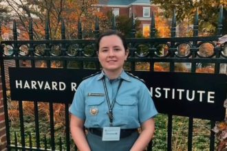 Oficial da Polícia Militar do Amazona ssorrindo em frente ao portão do Harvard Radcliffe Institute, usando uniforme.