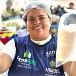 Mulher sorrindo segura sacos de grãos em feira regional de Manaus