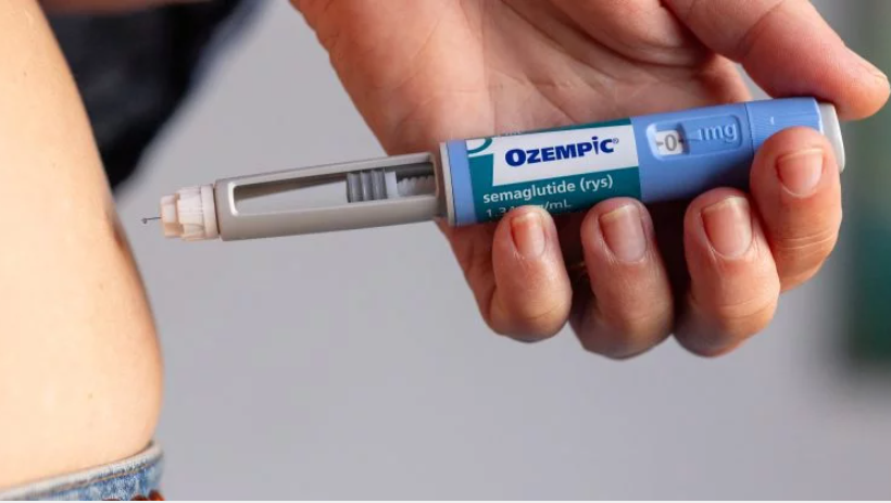 Injeção de Ozempic sendo aplicada no abdômen. Caneta injetora e pele visíveis.