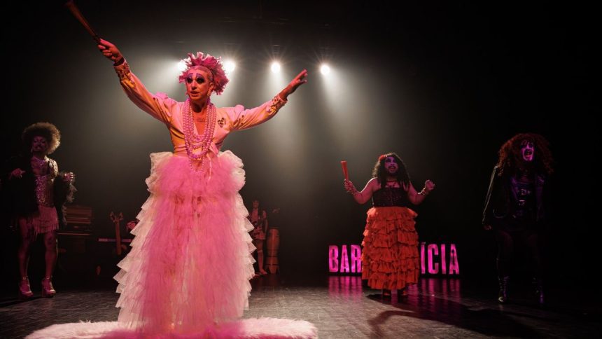 Performance drag no palco do festival, com figurinos elaborados e iluminação dramática.