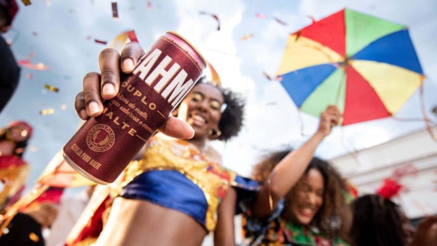 Pessoa segurando lata de cerveja Brahma Duplo Malte em celebração festiva com pessoas e guarda-chuva colorido.
