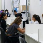 Pessoas em postos de atendimento, provavelmente em um local de trabalho ou escritório, com computadores.