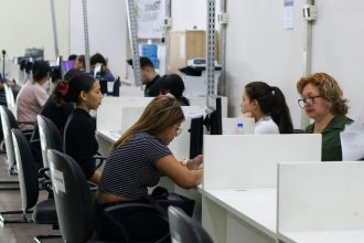 Pessoas em postos de atendimento, provavelmente em um local de trabalho ou escritório, com computadores.