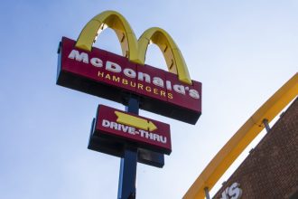 Placa do McDonald's com logotipo e letreiro 'Drive-Thru' em um dia ensolarado.