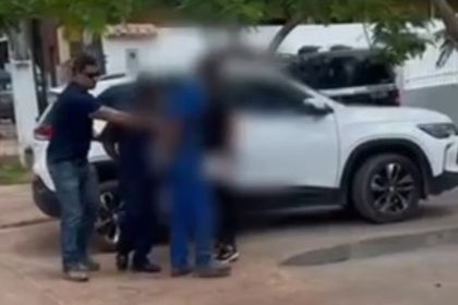 Policial conduz pessoas perto de um carro branco em investigação.