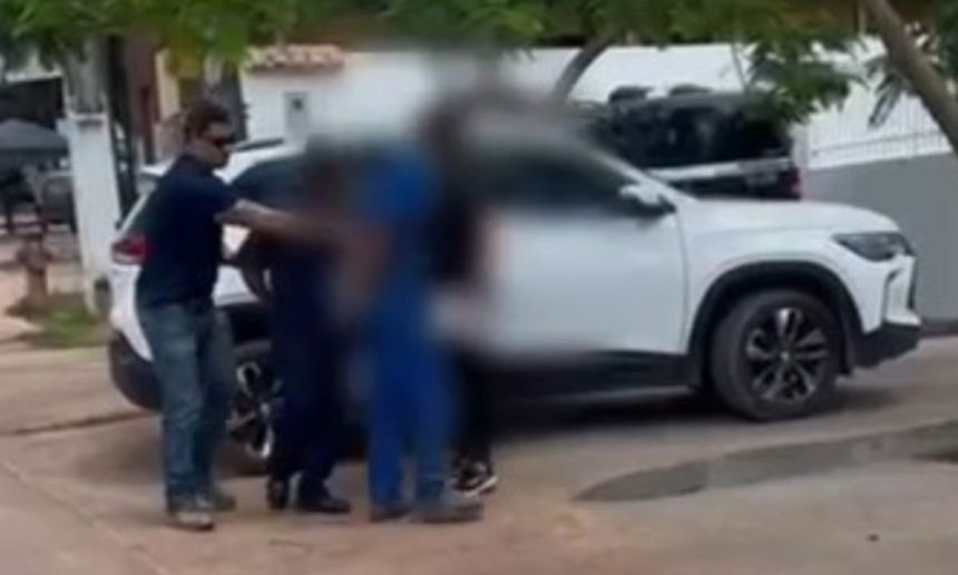 Policial conduz pessoas perto de um carro branco em investigação.