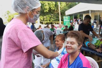 Profissional de saúde aplicando tratamento facial em mulher durante o Arena Rosa Azul, com outras pessoas ao fundo.