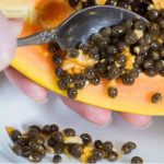 Removendo sementes de mamão com colher. Fruta cortada e sementes em tigela.