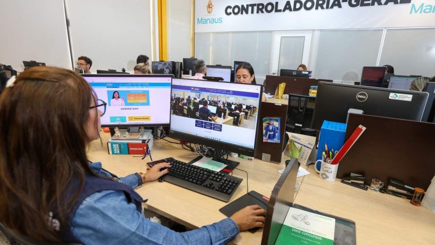 Servidores trabalhando em computadores em escritório, com destaque para telas mostrando o site da prefeitura de Manaus e um livro sobre concursos públicos.