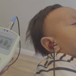 Teste de audição em bebê com equipamento Otodynamics, fones no ouvido e tela com resultados.