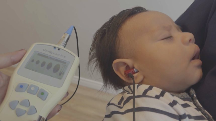 Teste de audição em bebê com equipamento Otodynamics, fones no ouvido e tela com resultados.