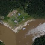 Vista aérea da confluência de rios na Amazônia, com edifícios e vegetação densa.