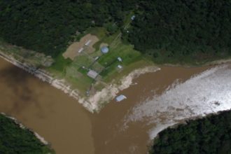 Vista aérea da confluência de rios na Amazônia, com edifícios e vegetação densa.