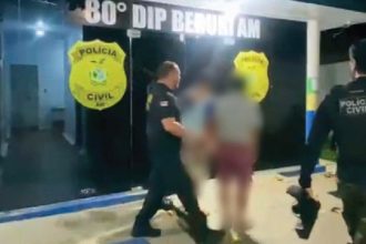 Polícia Civil conduz suspeitos para dentro da delegacia. Insígnia da polícia visível.