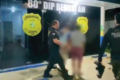 Polícia Civil conduz suspeitos para dentro da delegacia. Insígnia da polícia visível.