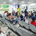 Sala de espera com pessoas sentadas em cadeiras de metal, aguardando atendimento em um centro de saúde.