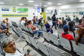Sala de espera com pessoas sentadas em cadeiras de metal, aguardando atendimento em um centro de saúde.