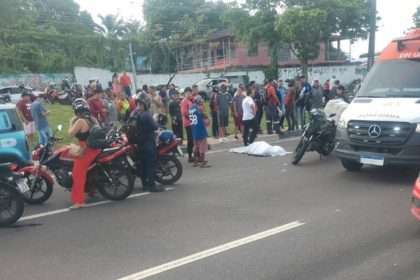 Acidente de trânsito com ambulância e pessoas reunidas. Motos e carro na cena.