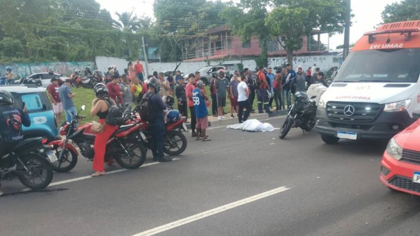 Acidente de trânsito com ambulância e pessoas reunidas. Motos e carro na cena.
