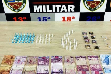Apreensão de drogas e dinheiro pela Polícia Militar. Itens apreendidos incluem pinos, embalagens e cédulas.