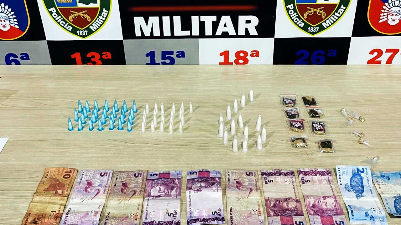 Apreensão de drogas e dinheiro pela Polícia Militar. Itens apreendidos incluem pinos, embalagens e cédulas.
