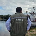 Homem de costas com colete Sema em frente a barco no rio, monitorando o meio ambiente.