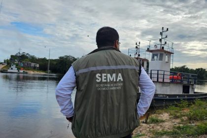 Homem de costas com colete Sema em frente a barco no rio, monitorando o meio ambiente.