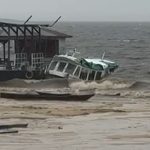 Lancha escolar danificado próximo a uma estrutura com cobertura, em meio a ondas.