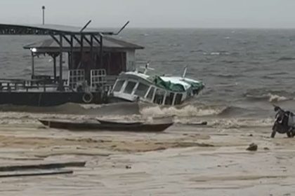 Lancha escolar danificado próximo a uma estrutura com cobertura, em meio a ondas.