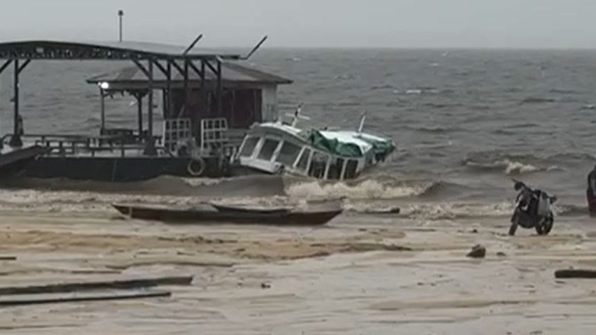 Lancha escolar danificado próximo a uma estrutura com cobertura, em meio a ondas.