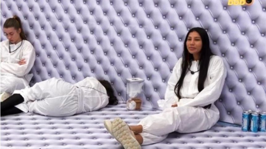 Participantes no interior da casa do Big Brother Brasil, vestindo macacões brancos, no quarto branco