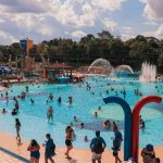 Piscina do Sesc lotada em um dia ensolarado, com pessoas nadando e se divertindo.