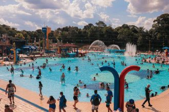 Piscina do Sesc lotada em um dia ensolarado, com pessoas nadando e se divertindo.