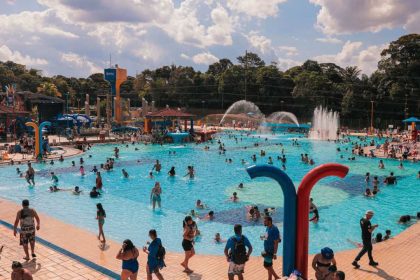 Piscina do Sesc lotada em um dia ensolarado, com pessoas nadando e se divertindo.