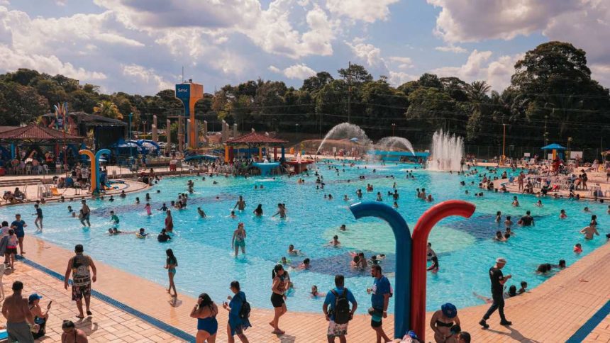 Piscina do Sesc lotada em um dia ensolarado, com pessoas nadando e se divertindo.