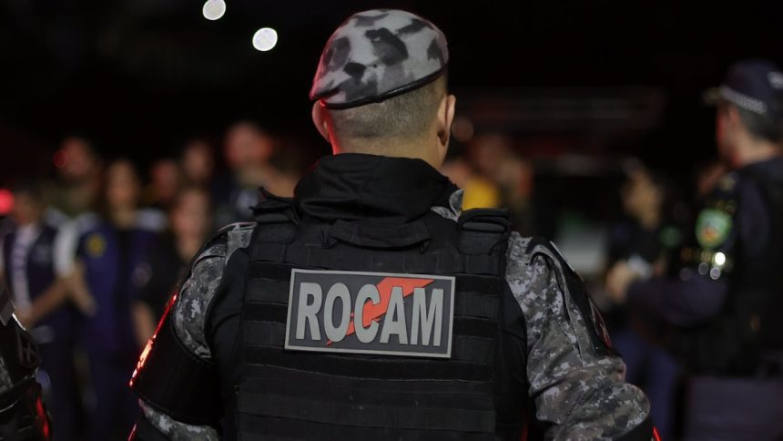 Policial militar de costas com uniforme camuflado e a palavra ROCAM no colete.