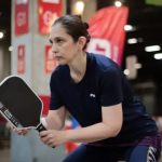 Mulher jogando pickleball em uma quadra interna, segurando uma raquete Joola.