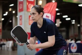 Mulher jogando pickleball em uma quadra interna, segurando uma raquete Joola.