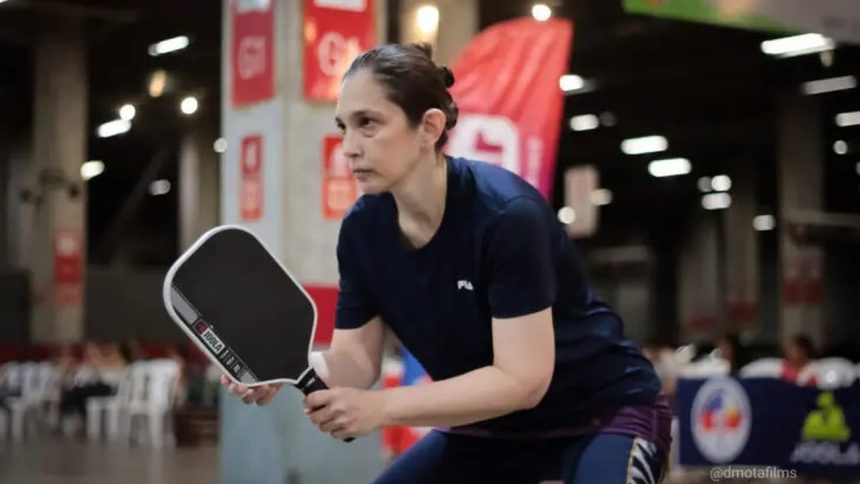 Mulher jogando pickleball em uma quadra interna, segurando uma raquete Joola.