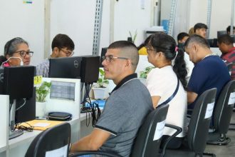 Pessoas sentadas em seus computadores em um ambiente de escritório, um local de atendimento e busca de emprego do Sine.