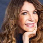 Elba Ramalho sorrindo com cabelo castanho ondulado e a mão no rosto
