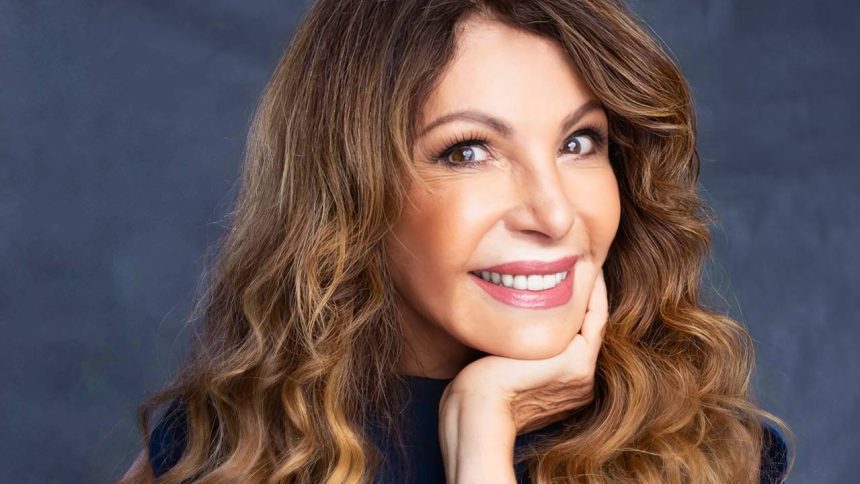 Elba Ramalho sorrindo com cabelo castanho ondulado e a mão no rosto