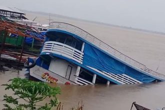 Barco parcialmente submerso em rio, com inclinação acentuada em Manacapuru